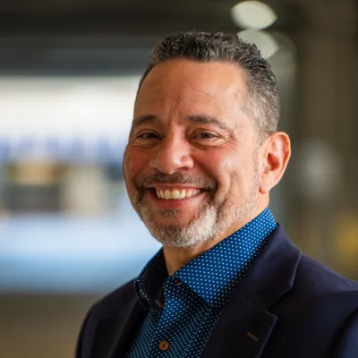 Smiling middle-aged man in a navy blazer and blue polka dot shirt in a softly blurred indoor setting