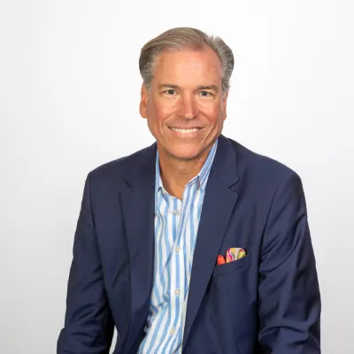 Middle-aged man in blue suit and striped shirt smiling against a plain white background.