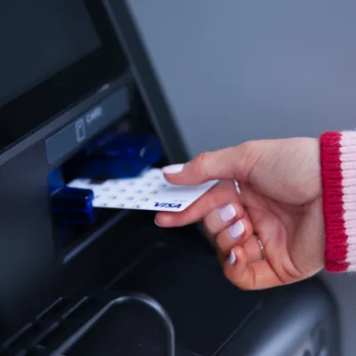 Close-up of a hand inserting a Visa card into an ATM machine slot with a pink sweater sleeve visible