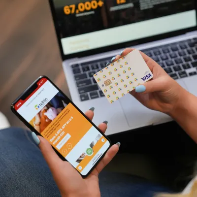 Person holding a Visa credit card and smartphone with banking app, laptop in the background for online payment.