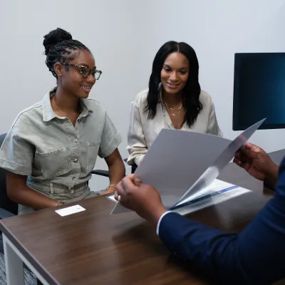 Two women attentively reviewing documents with a man in a professional office setting.