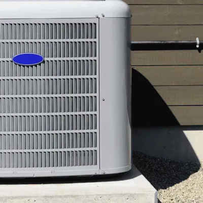 Outdoor air conditioning unit mounted on a concrete slab next to a wooden house exterior wall