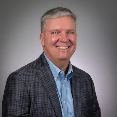 Smiling middle-aged man in a blue checkered blazer and light blue shirt against a gray background