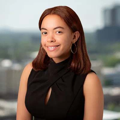 Young woman with shoulder-length red hair wearing a black sleeveless top smiling in an urban outdoor setting.