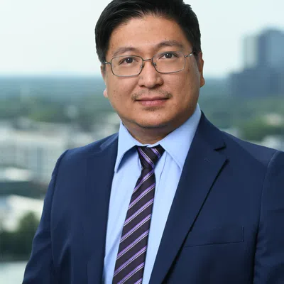Professional man in blue suit, striped tie, and glasses posing outdoors with cityscape background