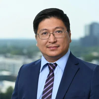 Professional man in blue suit, striped tie, and glasses posing outdoors with cityscape background