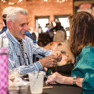 Two adults smiling and chatting across a table at an indoor social event in a cozy, well-lit space
