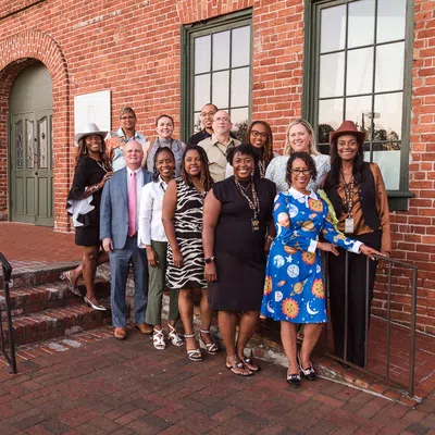 Diverse group of professionals posing outside a red brick building on stairs and sidewalk