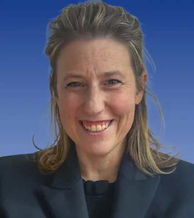 Smiling woman with light brown hair wearing a black blazer and black top against a blue background