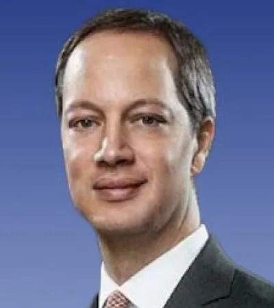 Portrait of a man wearing a dark suit and patterned tie against a blue gradient background.