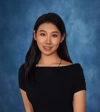 Portrait of a young woman with long black hair wearing a black off-shoulder top against a blue textured background