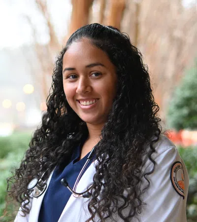 Smiling female medical student with curly hair wearing a white coat and stethoscope outdoors
