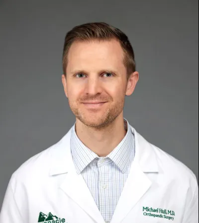 Smiling male doctor in white coat with Pinnacle Orthopaedics logo and Dr. Michael Hull name tag