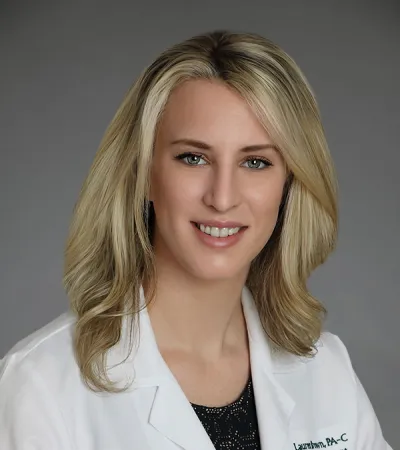 Female medical professional in a white coat with Pinnacle Orthopaedics logo and name tag, smiling against gray background.