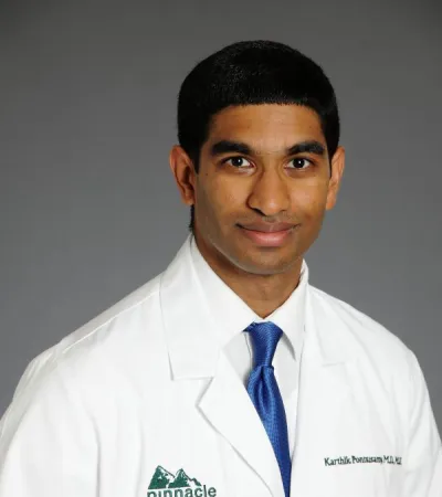 Professional portrait of a male doctor in a Pinnacle Orthopaedics white coat and blue tie against a gray background
