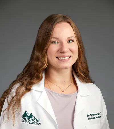Smiling female physician assistant in white coat with Pinnacle Orthopaedics logo on gray background