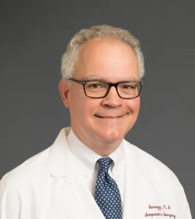 Smiling male doctor in glasses wearing Pinnacle Orthopaedics white coat and patterned blue tie on gray background