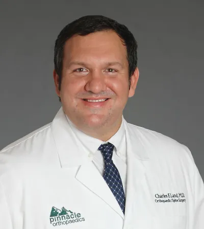 Smiling male doctor in white coat with Pinnacle Orthopaedics logo and name tag for orthopedic spine surgeon