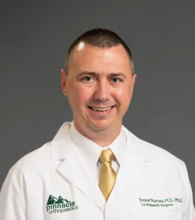 Smiling male orthopaedic surgeon in white coat and gold tie on gray background