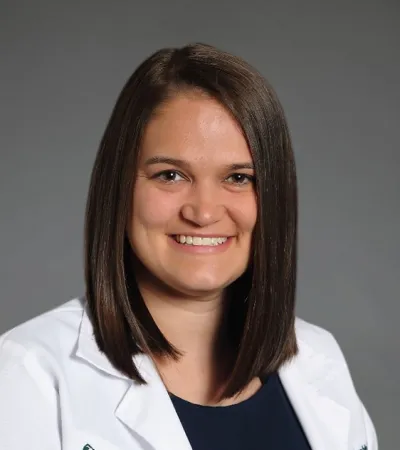 Professional woman with shoulder-length brown hair wearing a Pinnacle Orthopaedics white coat smiling on gray background