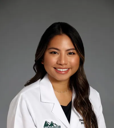 Smiling female doctor wearing a white Pinnacle Orthopaedics lab coat against a gray background.