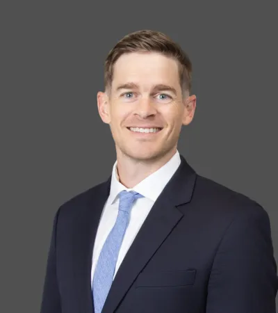 Portrait of a smiling man in a dark suit with a light blue tie against a gray background