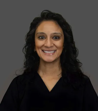 Smiling woman with curly black hair wearing a black top against a plain gray background.
