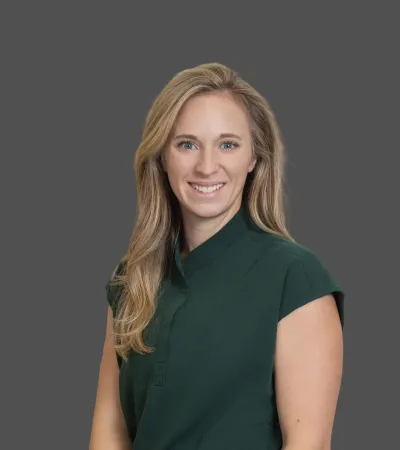 Smiling blonde woman in a dark green sleeveless top against a plain gray background.