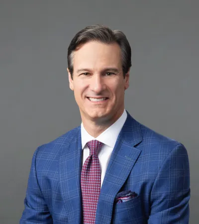 Smiling man in blue checkered suit and red tie posing against a plain gray background.