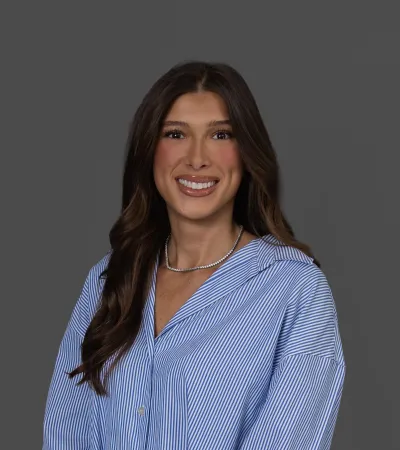 Smiling woman with long brown hair wearing a blue and white striped shirt against a gray background