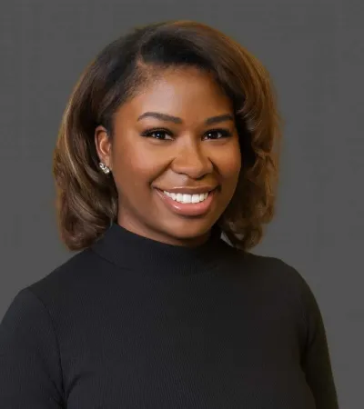 Smiling woman with shoulder-length hair wearing a black turtleneck against a gray background