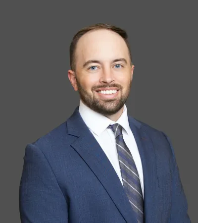 Smiling man with beard in a blue suit and striped tie on gray background professional headshot