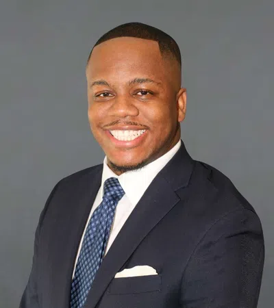 Smiling professional man in a dark suit and blue patterned tie against a plain grey background