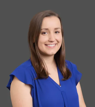 Smiling woman with brown hair wearing a blue blouse posing against a gray background