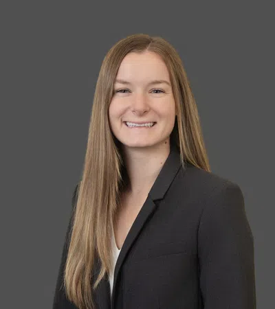 Portrait of a smiling woman with long straight hair wearing a dark blazer against a gray background