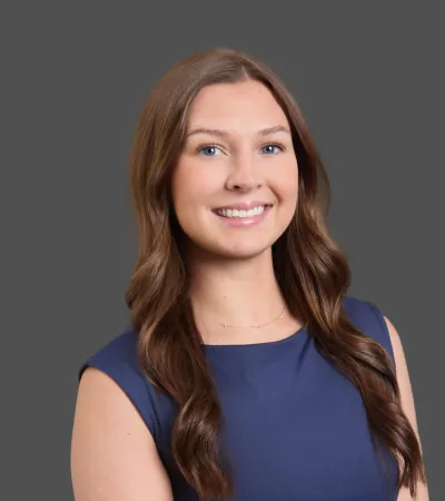 Smiling young woman with long brown hair wearing a blue sleeveless top against a gray background