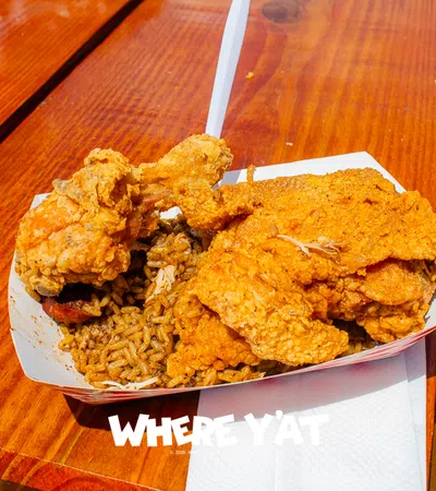 Tray with fried chicken pieces and seasoned rice on a wooden table with a plastic fork.