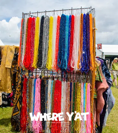 Colorful beaded necklaces hanging on a display rack at an outdoor market with people and tents in the background