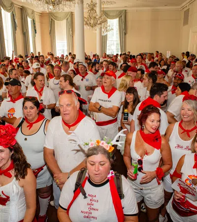 Large crowd dressed in white with red accessories gathers indoors celebrating a festive event.
