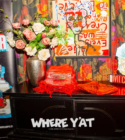 Colorful display with Live Louder banner, Mi Campo tequila bottles, floral vase, art, and Where Y'at signage on a black table.