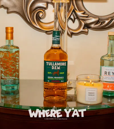 Five assorted liquor bottles and a lit French Vanilla candle displayed on a curved glass table with ornate metal wall decor.