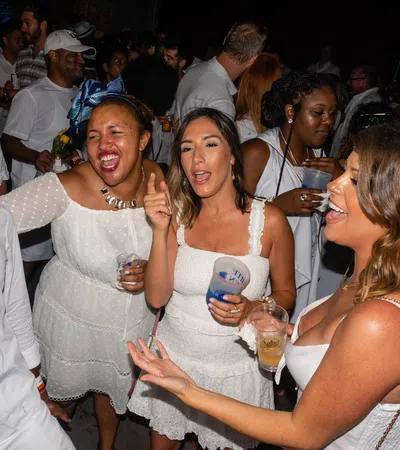 Group of friends in white outfits enjoying lively party with drinks and dancing at night event.