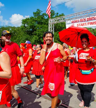 Participants in red dresses enjoy the NOH3 Red Dress Run at the start/finish line under a sunny sky.
