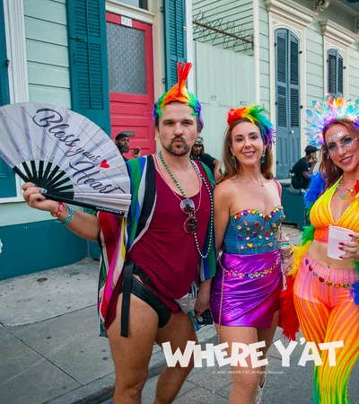Four colorful, lively people in festive rainbow outfits posing on a New Orleans street during a celebration.