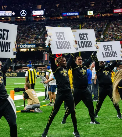 New Orleans Saints cheerleaders and dancers holding Get Loud signs on the football field during a game.
