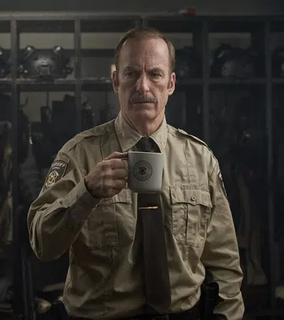 Police officer in uniform holding a white mug inside an armory with helmets and gear in the background