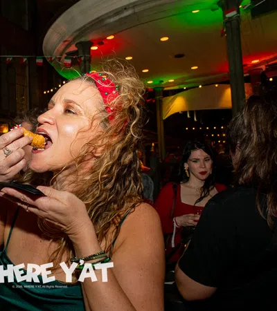 Woman in red headband eating fried food at lively nighttime party with people drinking and socializing.