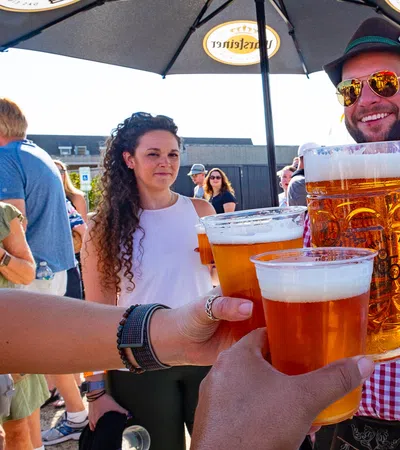 Group of people clinking large beer mugs and cups at an outdoor festival under branded umbrellas