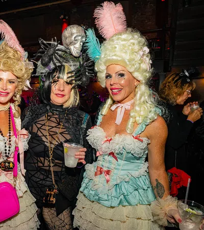 Four women in elaborate Halloween costumes with wigs and accessories at a festive party indoors.