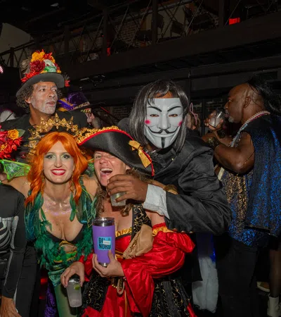 Group of adults in colorful and creative costumes posing indoors at a lively Halloween or costume party.